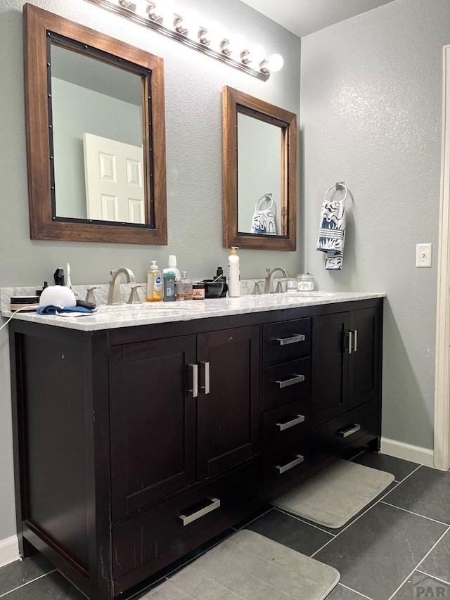 bathroom featuring baseboards, tile patterned flooring, a sink, and double vanity