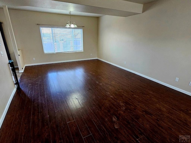spare room featuring wood-type flooring, baseboards, and a notable chandelier