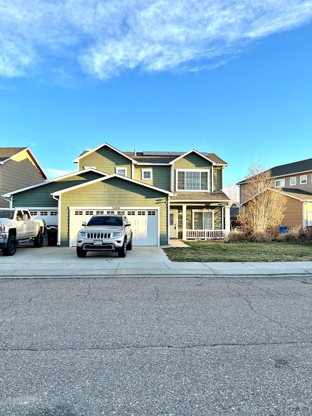 traditional-style house with roof mounted solar panels, an attached garage, covered porch, and driveway