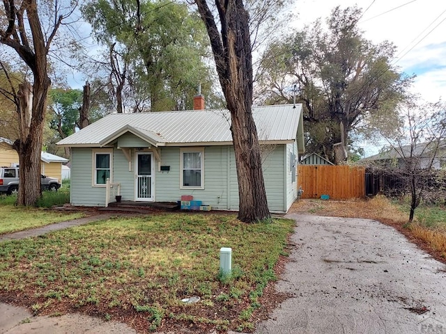 ranch-style house featuring driveway, a front lawn, fence, and metal roof