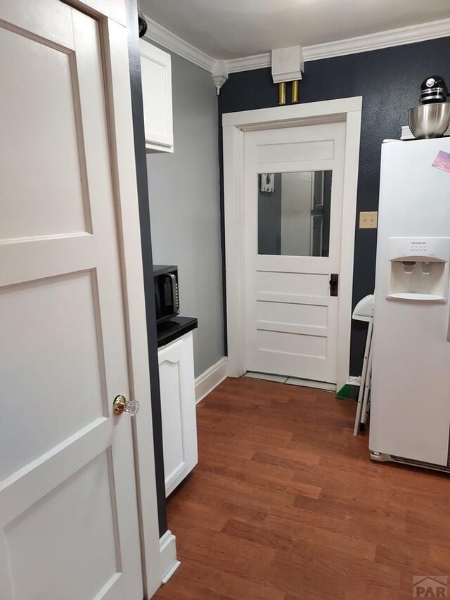 interior space with black microwave, white refrigerator with ice dispenser, white cabinets, dark wood finished floors, and crown molding