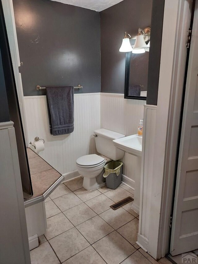 bathroom featuring tile patterned flooring, a wainscoted wall, visible vents, and toilet