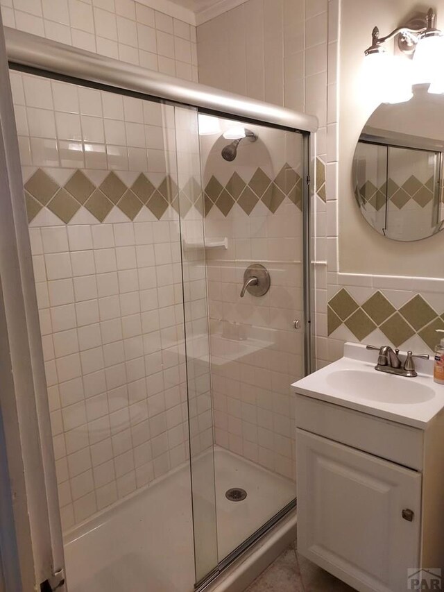 full bathroom with tasteful backsplash, a tile shower, vanity, and tile walls