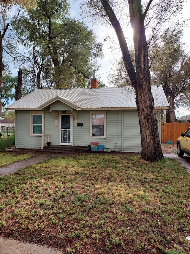 ranch-style home with a chimney, fence, metal roof, and a front yard