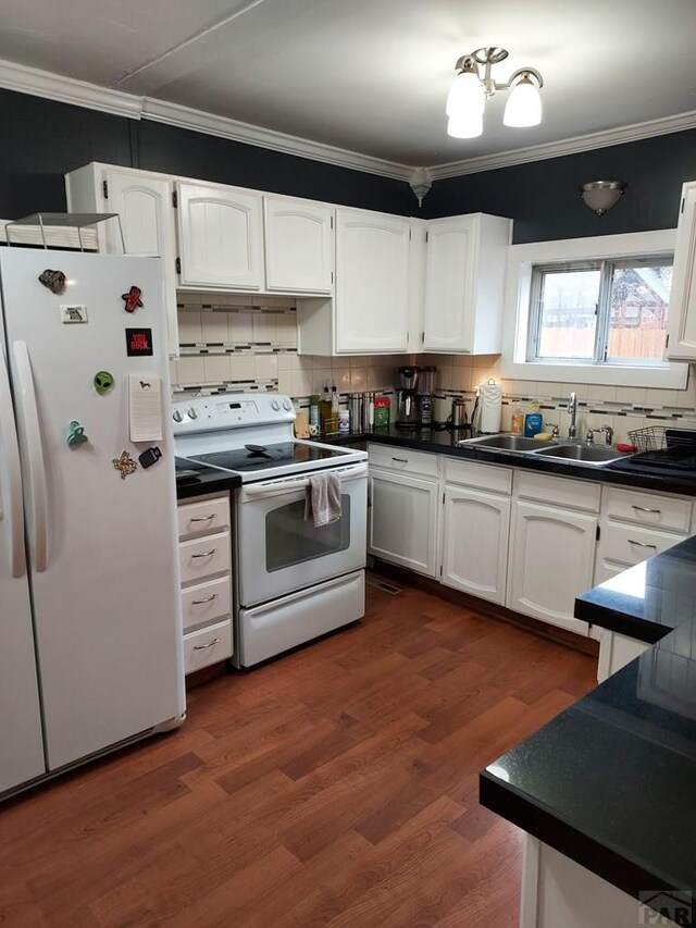 kitchen with white appliances, white cabinets, dark countertops, crown molding, and a sink