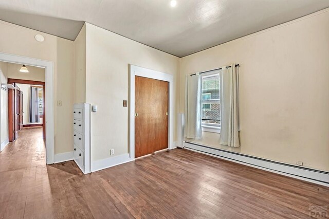 unfurnished bedroom featuring baseboards, a baseboard heating unit, and dark wood finished floors