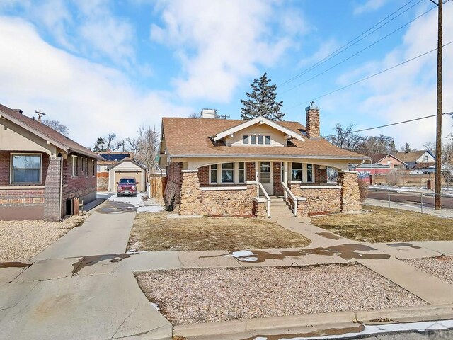 bungalow-style home featuring an outbuilding, a chimney, a porch, stone siding, and driveway