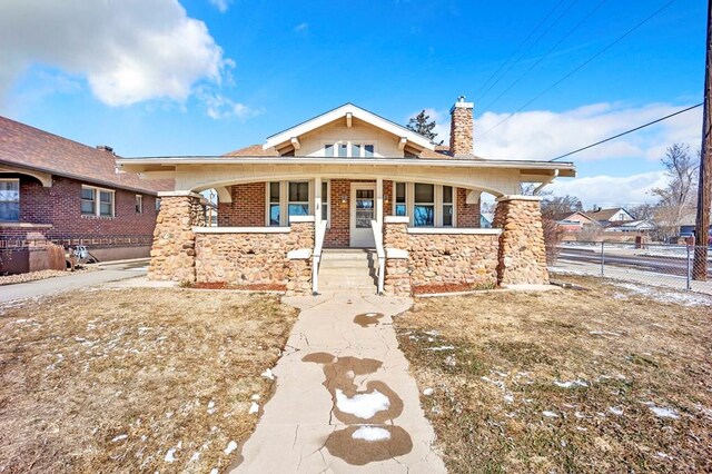 view of front facade featuring covered porch, brick siding, fence, and a chimney