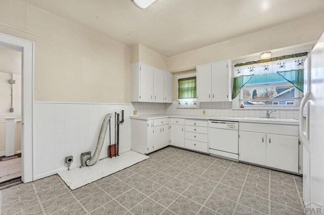 kitchen featuring a wainscoted wall, light countertops, white cabinetry, a sink, and dishwasher