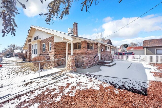 view of snowy exterior with a chimney, fence, and brick siding