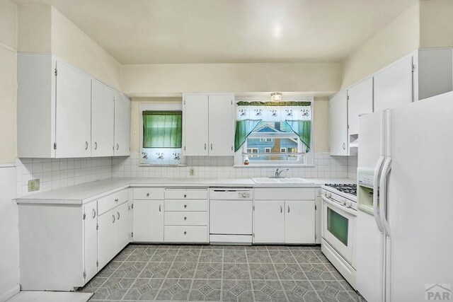 kitchen featuring light countertops, decorative backsplash, white cabinetry, a sink, and white appliances