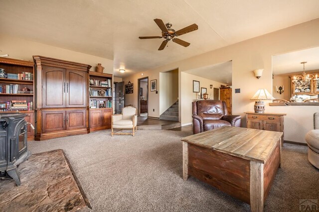 living area featuring ceiling fan, baseboards, stairway, dark colored carpet, and a wood stove