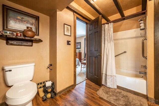 bathroom with baseboards, wood finished floors, toilet, and shower / bathtub combination with curtain