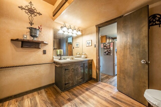 bathroom featuring a textured wall, baseboards, wood finished floors, and vanity