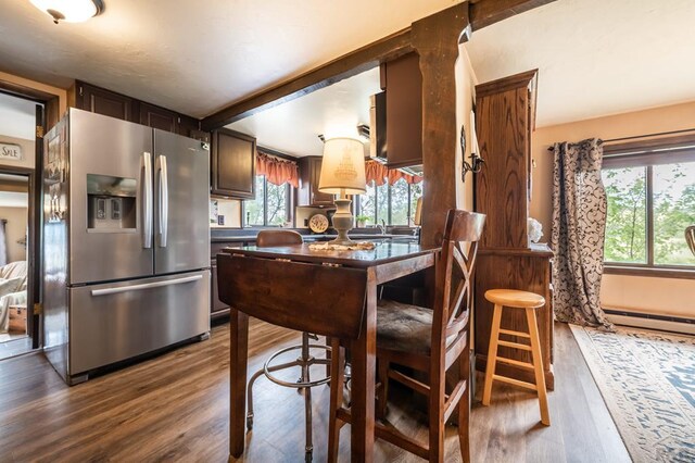 kitchen featuring dark brown cabinetry, a baseboard heating unit, wood finished floors, stainless steel refrigerator with ice dispenser, and beamed ceiling