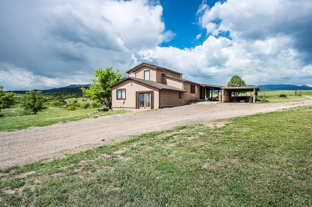 view of front of house with dirt driveway, a mountain view, a front lawn, and a carport