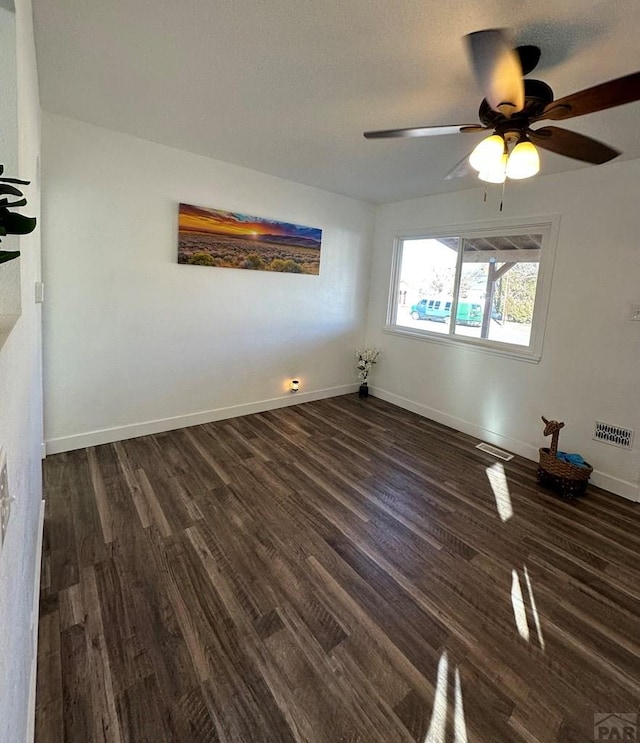 spare room with dark wood-type flooring, visible vents, and baseboards