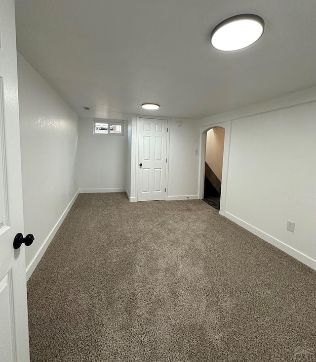 below grade area featuring baseboards, arched walkways, and carpet flooring