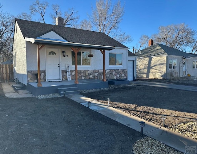 view of front of property featuring a shingled roof, stone siding, a chimney, a porch, and stucco siding