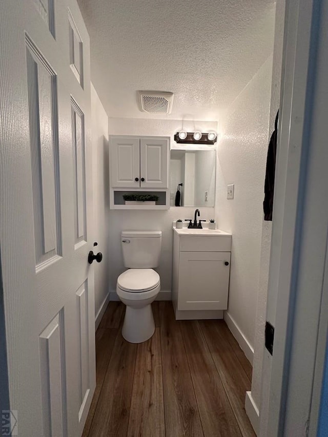 half bathroom with a textured ceiling, toilet, wood finished floors, vanity, and baseboards