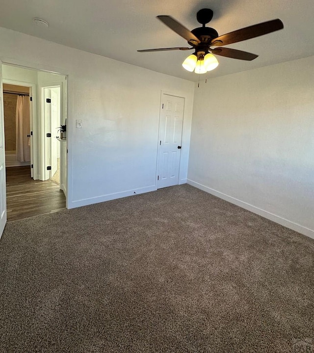 empty room with a ceiling fan, dark colored carpet, and baseboards