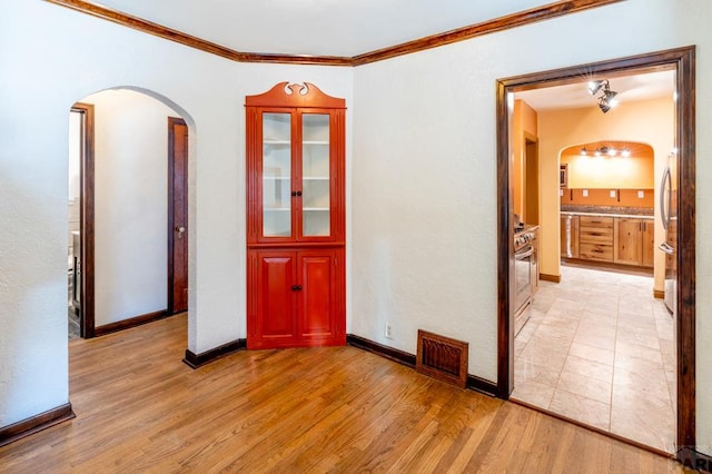 spare room with arched walkways, visible vents, light wood-style floors, ornamental molding, and baseboards