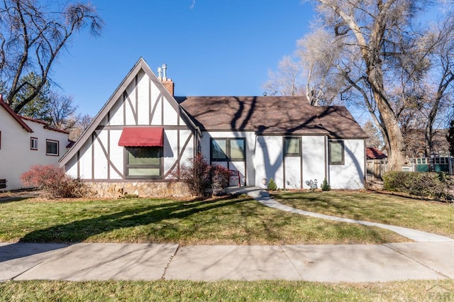 tudor house featuring a front lawn, a chimney, and stucco siding