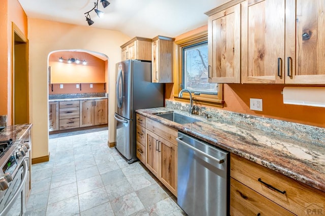 kitchen with stone countertops, appliances with stainless steel finishes, vaulted ceiling, and a sink