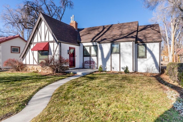 tudor-style house with a front yard, a chimney, and stucco siding