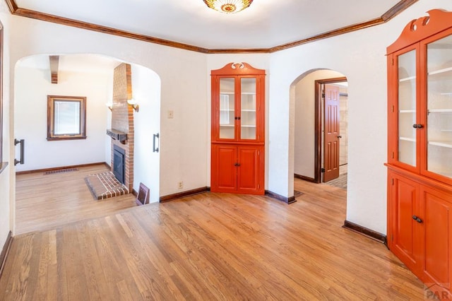 spare room with light wood-type flooring, a brick fireplace, crown molding, and arched walkways