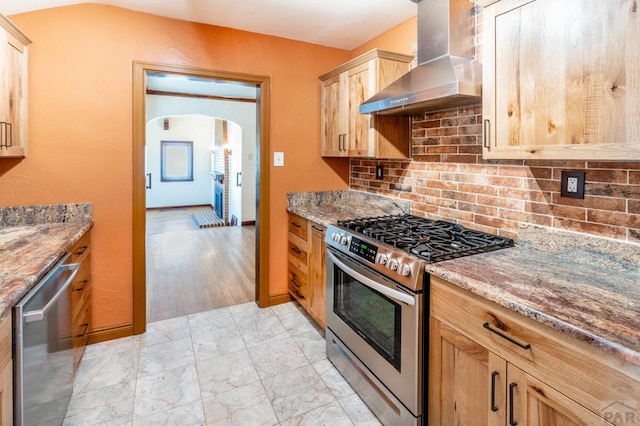 kitchen with wall chimney exhaust hood, light brown cabinetry, light stone counters, and stainless steel appliances