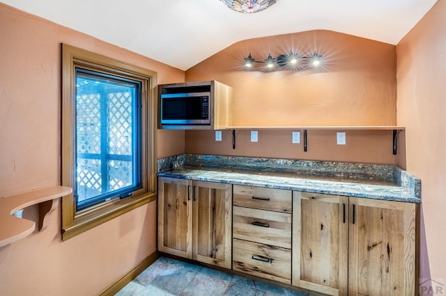 kitchen featuring stainless steel microwave, vaulted ceiling, and baseboards