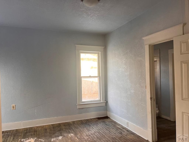 empty room with a textured ceiling, baseboards, hardwood / wood-style flooring, and a textured wall