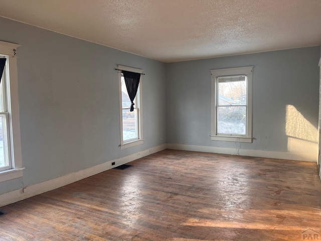 unfurnished room featuring plenty of natural light, wood finished floors, and visible vents