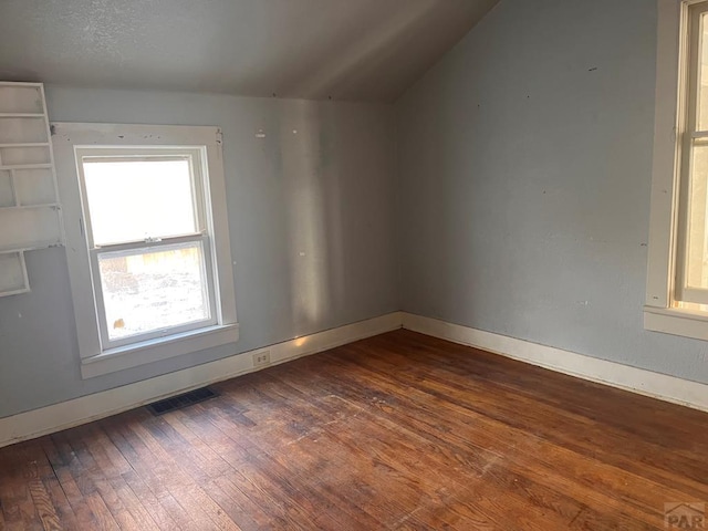 empty room featuring lofted ceiling, dark wood-style floors, visible vents, and baseboards