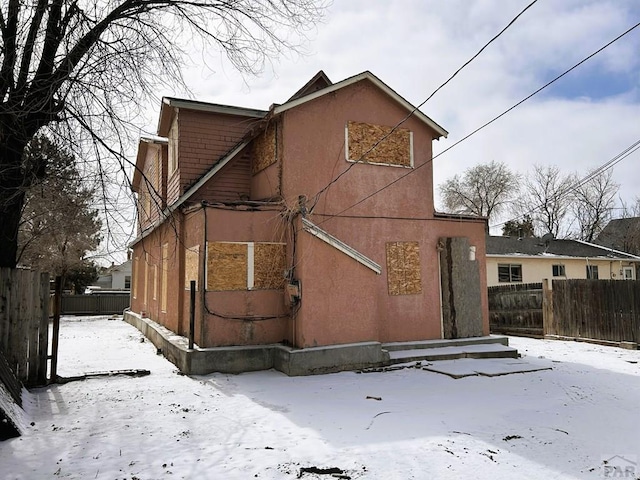 snow covered rear of property featuring fence and stucco siding