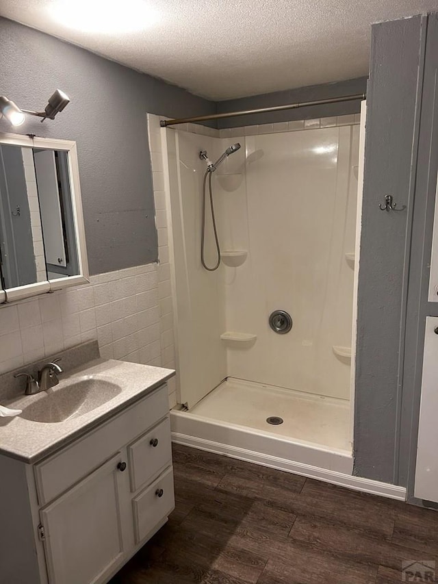 bathroom with tile walls, a stall shower, vanity, a textured ceiling, and wood finished floors