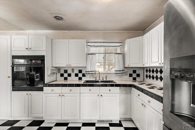 kitchen featuring tile counters, white cabinets, black oven, and a sink