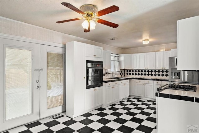 kitchen featuring tile countertops, dark floors, stainless steel appliances, a sink, and white cabinetry