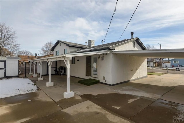 rear view of house featuring stucco siding, a storage unit, an attached carport, an outdoor structure, and driveway