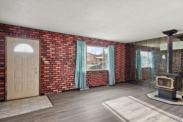 entryway with a wood stove, a textured ceiling, brick wall, and wood finished floors