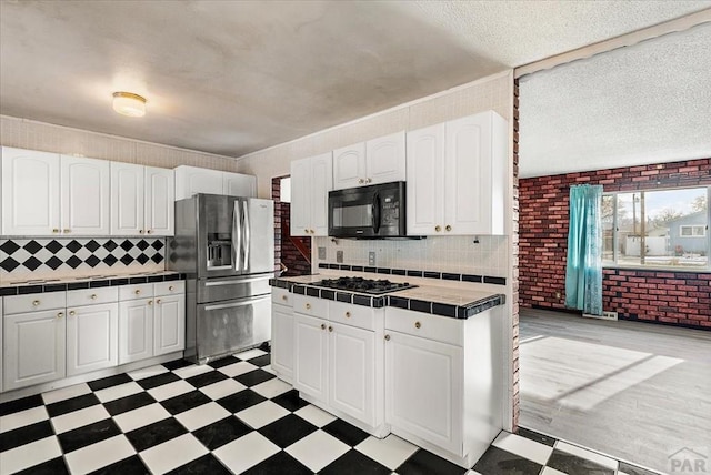 kitchen with light floors, tile counters, white cabinetry, black microwave, and stainless steel fridge