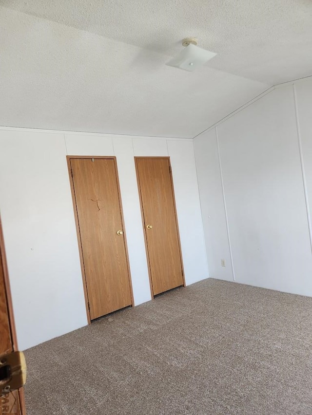 unfurnished bedroom featuring carpet floors, vaulted ceiling, a textured ceiling, and multiple closets