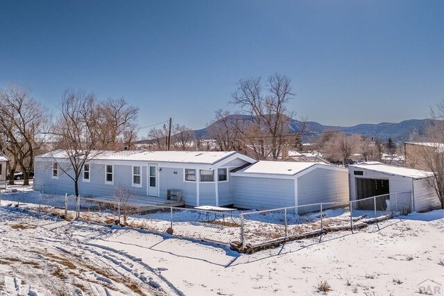 snow covered rear of property featuring an outbuilding, fence, a mountain view, and a garage