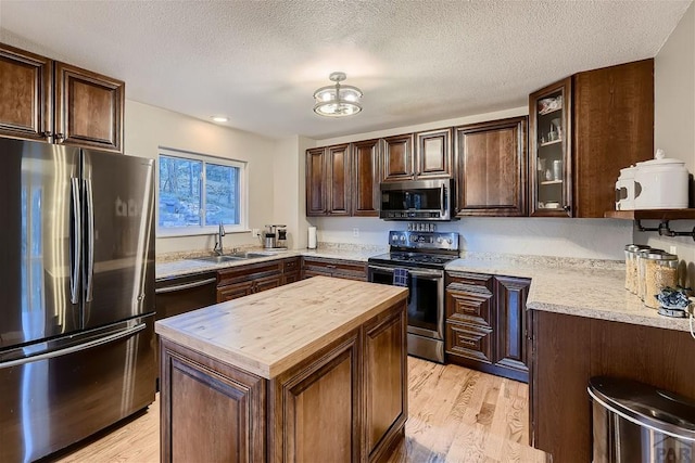 kitchen with light wood-style flooring, glass insert cabinets, appliances with stainless steel finishes, wooden counters, and a sink