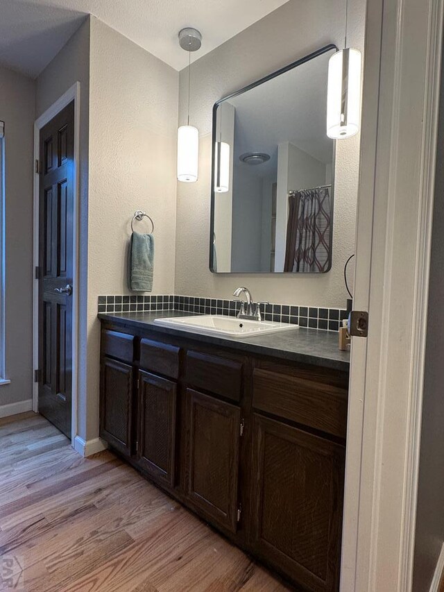 full bathroom featuring a textured wall, wood finished floors, vanity, and baseboards