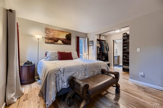 bedroom with a spacious closet, light wood-type flooring, and baseboards