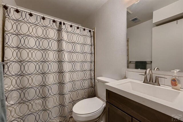 full bath featuring curtained shower, visible vents, a textured wall, toilet, and vanity