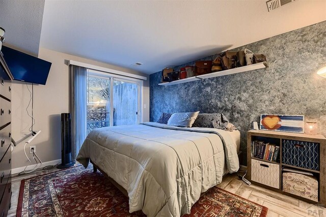 bedroom with an accent wall, wood finished floors, visible vents, baseboards, and wallpapered walls