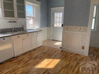 kitchen with a wainscoted wall, a sink, wood finished floors, dishwasher, and wallpapered walls